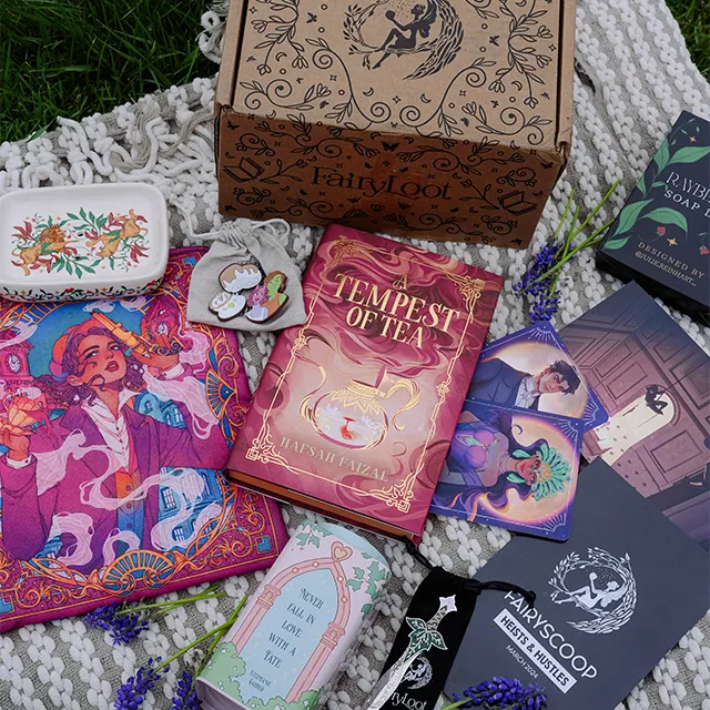 Présentation d'une box Fairyloot avec un livre aux tranches jaspées et des goodies de fantasy.